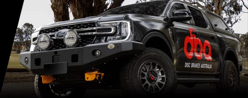 Pickup truck sombre brandé DBA Disc Brakes Australia avec logo DBA rouge et équipement éclairage supplémentaire en environnement extérieur