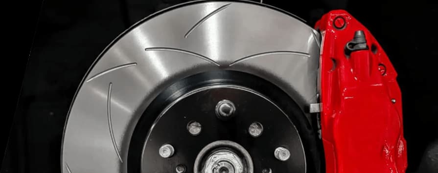 Gros plan d'un disque de frein rainuré DBA installé avec un étrier rouge vif sur un moyeu de véhicule