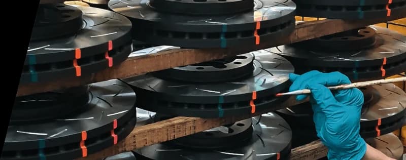 Technicien en gants bleus inspectant des disques de frein rainurés DBA empilés avec marquages indicateurs de température lors du contrôle qualité