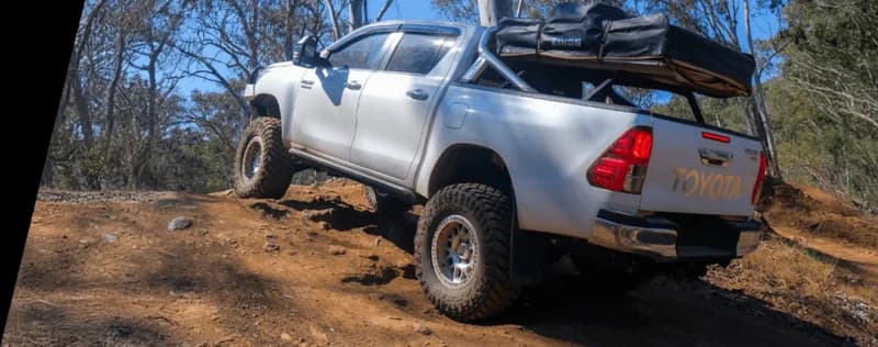 Pickup truck Toyota blanc chargé d'équipement camping positionné sur terrain rocheux en brousse australienne démontrant conditions tout-terrain charge lourde