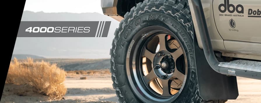 DBA 4000 Series Améliorations Freins 4x4 - Performance Tout-Terrain Gros plan roue véhicule 4WD sur terrain désertique avec branding DBA 4000 Series bien visible sur carrosserie, démontrant performance freinage tout-terrain