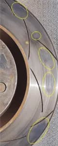Disque de frein avec dépôts visibles de matériau de friction pouvant entraîner des vibrations du volant et un freinage irrégulier Gros plan de la surface d'un disque de frein montrant des dépôts irréguliers de matériau de friction mis en évidence par des cercles jaunes