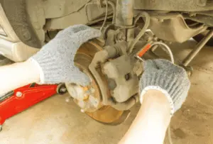 Technique correcte pour ouvrir la vis de purge d'étrier avec une clé et un tube de collecte pendant la procédure de purge des freins Mains gantées de mécanicien ouvrant la vis de purge d'étrier avec une clé tandis qu'un tube transparent est fixé pour capturer le liquide