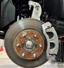 Étape 1A: Ensemble de frein d'origine montrant le disque et l'étrier qui seront remplacés lors de la procédure de mise à niveau DBA Gros plan de l'ensemble de frein d'origine montrant la surface du disque rouillée, l'étrier et le support avant l'installation de la mise à niveau DBA